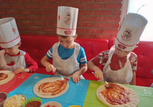 Chłopcy smarują sosem ciasto na pizzę