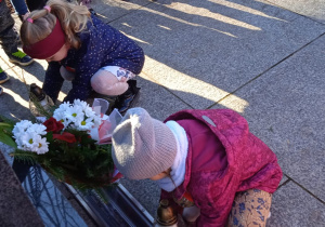 Dzieci ustawiają znicze pod pomnikiem