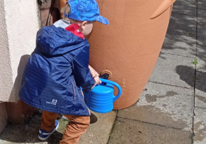 Chłopiec nalewa deszczówkę do konewki