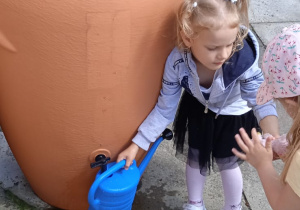 Dziewczynka nalewa deszczówkę do konewki