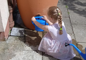Dziewczynka nalewa deszczówkę do konewki